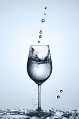 Transparent water pouring into wineglass while standing on the glass with water bubbles against light background.