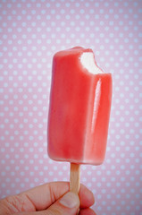 red strawbery ice lolly kept in hand over pink background 