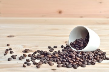 coffee beans from the white ceramic cup on wooden background