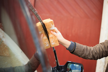 Young woman hands cleaning red car by yellow sponge, using a  detergent (color toned image)