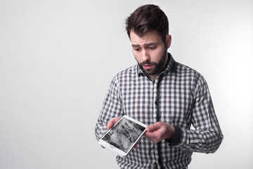 Bearded upset man holds a out-of-use tablet or smartphone. Isolated on a light background