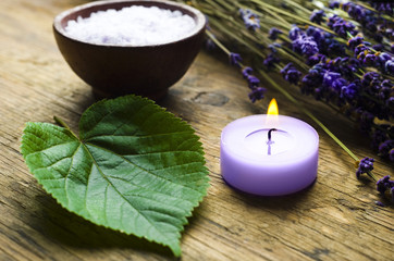 Lavender wellness concept with lavender plants, bowl of salt, a purple candle, green leaf over old wood background 
