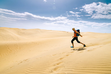 Man with a backpack runs on hot yellow sand in the desert, Canary Islands, Spain