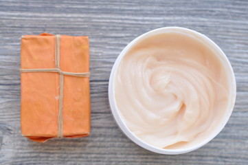 Large white can of body cream and handmade soap with orange packaging on a wooden surface

