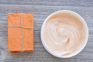Large white can of body cream and handmade soap with orange packaging on a wooden surface

