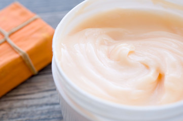 Large white can of body cream and handmade soap with orange packaging on a wooden surface
