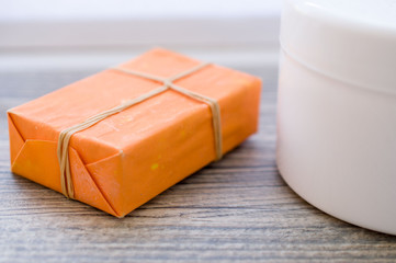 Large white can of body cream and handmade soap with orange packaging on a wooden surface

