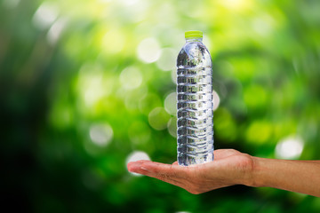 Man's hand holding drinking water bottle on blurred redial green bokeh background