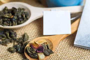 Tea in a glass cup with Dry (black and green) tea in wooden spoons, Herbal teabags on burlap tablecloths. 
