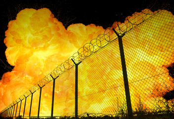 Realistic orange fire explosion behind restricted area barbed wire fence