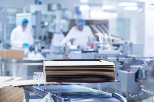 Workers on production line in pharmaceutical plant, cardboard boxes stacked in foreground