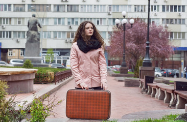 Alone girl staying on empty street with retro suitcase. Big city loneliness