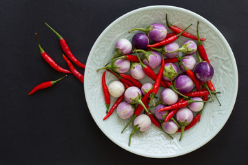 Purple Thai eggplants and hot chili peppers on a green plate and nearby on a black background. Asian food.