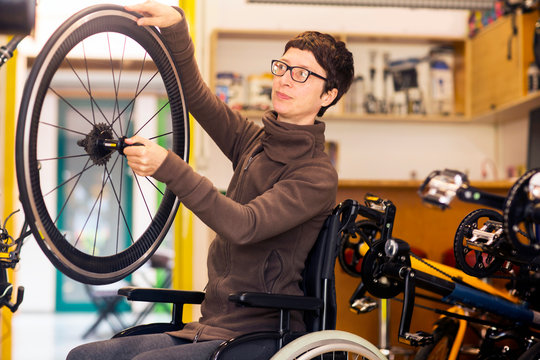 Woman in wheelchair in bicycle repair shop, holding bicycle wheel
