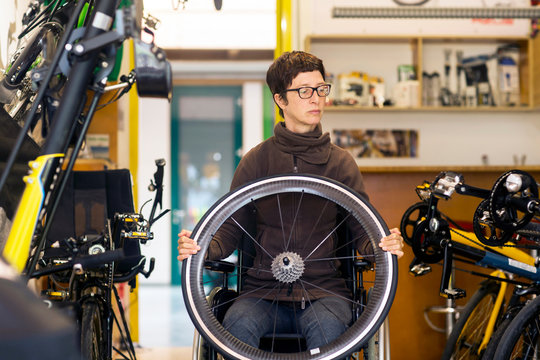 Woman in wheelchair in bicycle repair shop, holding bicycle wheel