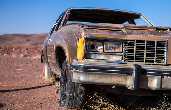 Old Brown Car With A Busted Headlight And Flat Tire In The Desert Under A Blue Sky