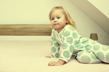 Fototapeta premium Two small identical twin sisters in identical pajamas, actively having fun on the parent's bed,