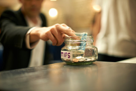 Close up of businessman putting cash into barber shop gratuity jar