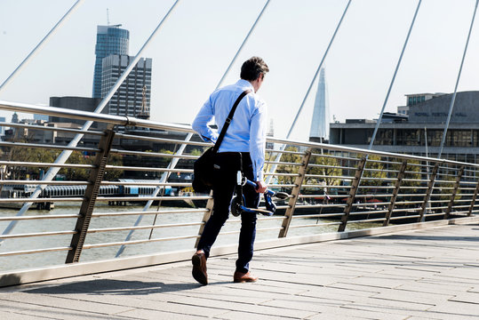 Businessman carrying scooter, Hungerford Bridge, London, UK