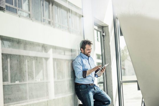 Businessman leaning against office lobby wall using digital tablet touchscreen