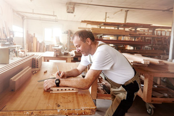 Male carpenter marking wood with pencil at workbench