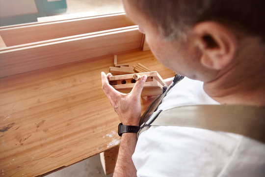 Over shoulder view of carpenter inserting wooden dowel at workbench
