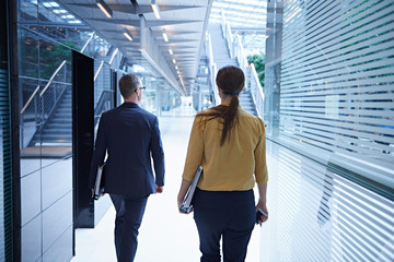 Rear view of businesswoman and man walking through office atrium