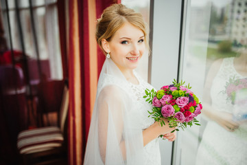 Wedding. Wedding day. Beauty bride in bridal gown with bouquet and lace veil indoors. Beautiful model girl in a white wedding dress. Female portrait of cute lady. Woman with hairstyle