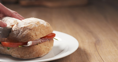 man cuts ciabatta sandwich with speck, mazzarella and vegetables, 4k photo