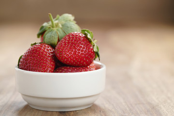 ripe organic strawberries in white bowl on wood table, with copy space