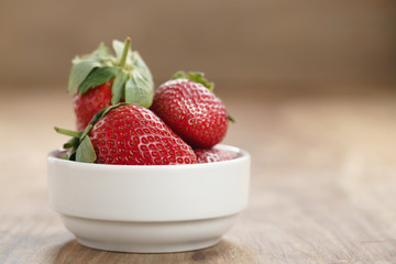 ripe organic strawberries in white bowl on wood table, with copy space