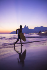 Scenic sunset view of Ipanema Beach in Rio de Janeiro, Brazil with the silhouette of a skimboarder running across the shore in motion blur