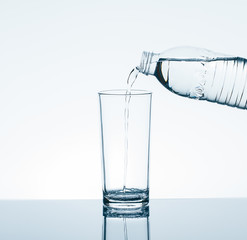 Pouring drinking water from bottle into drinking glass on white background