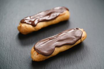 two eclairs with dark chocolate on top on slate background, shallow focus