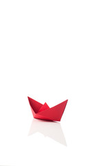 Red paper ship on white with reflection