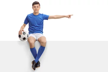 Gordijnen Teenage football player sitting on a panel and pointing right © Ljupco Smokovski