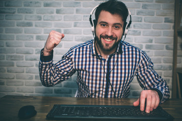 Bearded man playing at home and streaming. Funny guy is excited because of seen virtual video. He is wearing red headphones