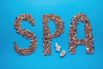 Inscription (word, sign) 'Spa' made of seashells on blue paper background,