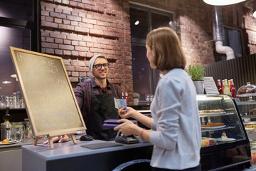 Fototapeta premium happy barman and woman paying money at cafe