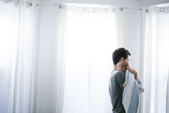 Mid adult man carrying baby son in living room