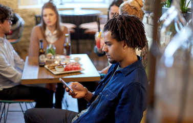 man with smartphone and friends at restaurant