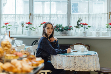 Attractive young woman sitting at table and looking on the showcase with delicious sweets. Healthy, diet and lose weight concept