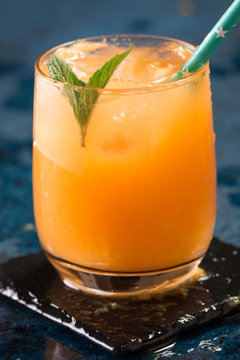 Orange juice in glass with mint, fresh fruits on dark blue background