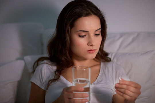 woman with pill and glass of water in bed at home