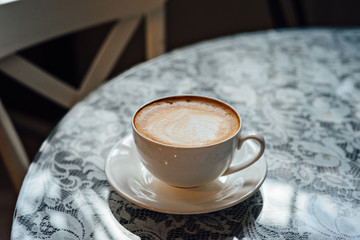 Cup of cappuccino on the table with lace tablecloth.