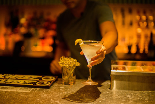 Bar tender serving cocktail drink over bar