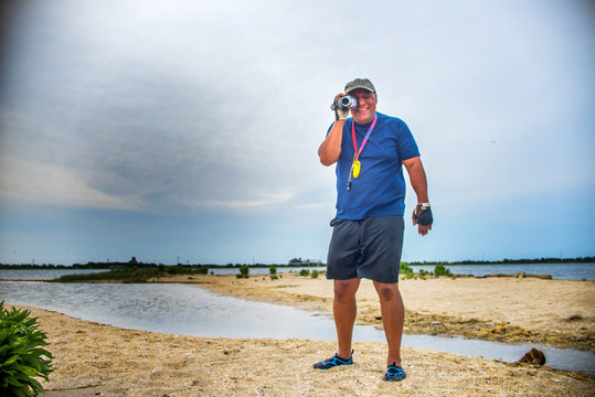Mature man standing on beach looking through camcorder