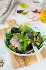 Salad with fresh radishes, arugula, beets, chard, sunflower seeds, flax and sesame seeds on a light background. Selective focus. top view. Copy space.