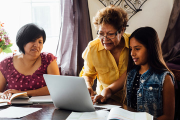 Mother and grandmother helping girl with homework using laptop