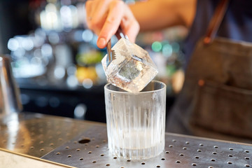 bartender adding ice cube into glass at bar